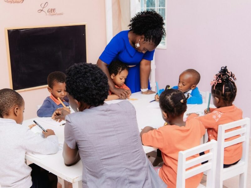 A teacher guides young children drawing at a classroom table