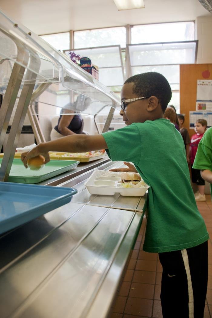 A student chooses food items in an elementary school cafeteria lunch line